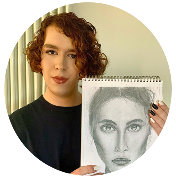 A young person with short red hair wearing makeup and pink lipstick. They're wearing a navy t-shirt and they're holding a black and white sketched drawing to the left of them.