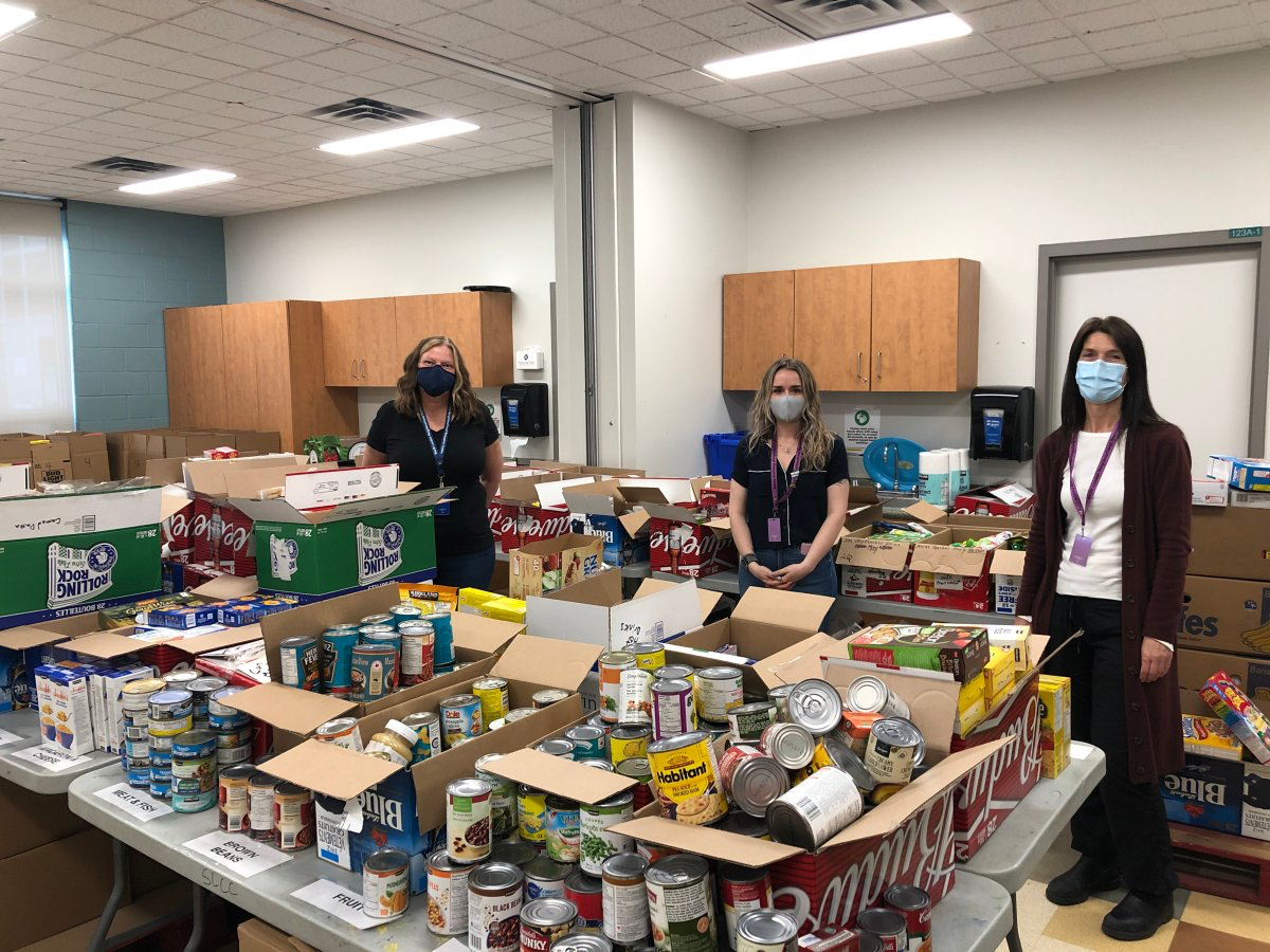 A group of people wearing face masks standing in a room with food boxes  Description automatically generated